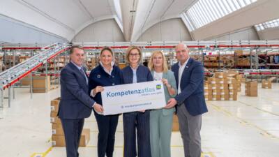 Menschen halten ein Schild zum NÖ Kompetenzatlas in einer Lagerhalle
