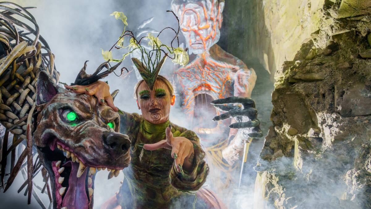 Kostümierte Frau mit aufwendigem Gesichtsschmuck neben einem Drachenkopf und Gruselkulissen