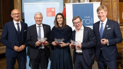 Fünf Personen präsentieren gläserne Auszeichnungen vor Club-Tirol- und Tirol-Land-Bannern.