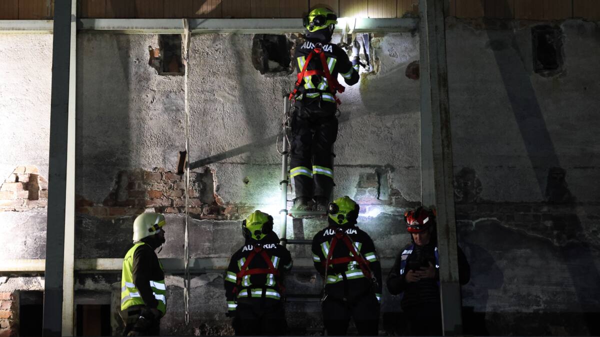 Einsatzkraft mit Helm und Sicherungsgurt untersucht eine beschädigte Wand bei einer Übung.