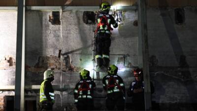 Einsatzkraft mit Helm und Sicherungsgurt untersucht eine beschädigte Wand bei einer Übung.