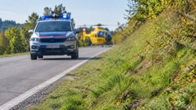 Ein gelber Rettungshubschrauber steht hinter einem Einsatzfahrzeug an einer Landstraße.