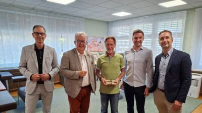Wilfried Fritz steht mit vier Stadtvertretern in einem Büro und hält einen kleinen Gegenstand.