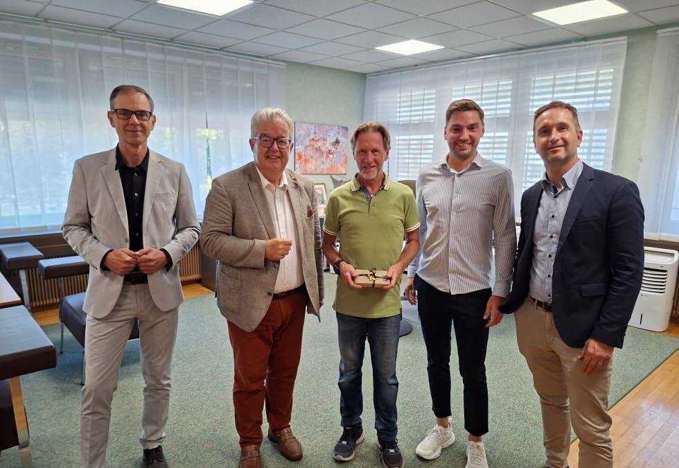 Wilfried Fritz steht mit vier Stadtvertretern in einem Büro und hält einen kleinen Gegenstand.