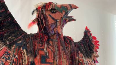 Farbenfrohe textile Skulptur eines vogelartigen Wesens mit ausgebreiteten Flügeln