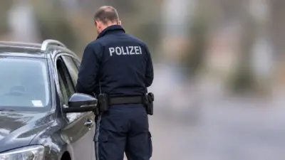 Ein Polizist in Uniform steht mit dem Rücken zur Kamera neben einem Auto.
