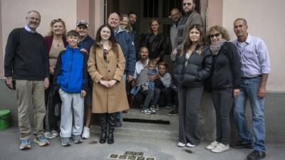 Eine Gruppe steht vor einem Hauseingang; davor liegen sieben Stolpersteine.