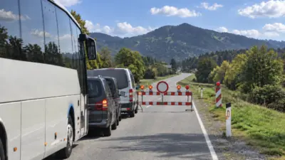 Bus und Fahrzeuge vor einer Straßensperre auf einer Straße in alpiner Landschaft