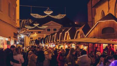 Menschen besuchen beleuchtete Marktstände unter festlicher Straßenbeleuchtung