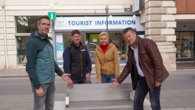 Personen stehen neben einer massiven Betonbank vor einer Touristeninformation.