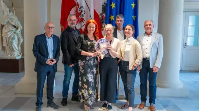 Eine Gruppe posiert vor Flaggen und hält gemeinsam eine runde Plakette.