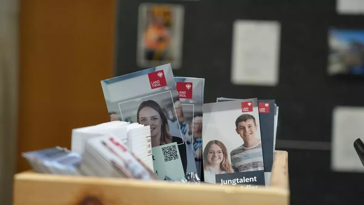 In einer Holzbox stehen Broschüren mit dem Land-Tirol-Logo und Porträtfotos.