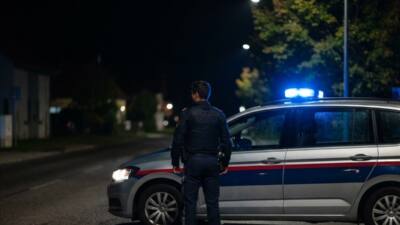 KI-generiertes Bild: Ein uniformierter Mann steht nachts neben einem silbernen Auto mit Blaulicht.