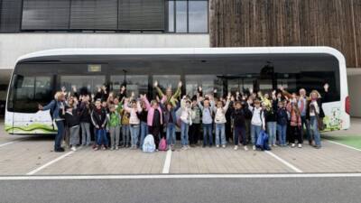 Eine Schülergruppe winkt vor einem Bus; die KMG erprobt in Klagenfurt einen Elektrobus im Alltag.