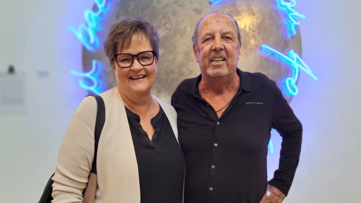 Eine Frau und ein Mann lächeln vor einer blau leuchtenden Kunstinstallation.