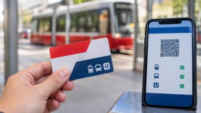 Eine Hand hält eine Fahrkarte neben einem Smartphone mit QR-Code; dahinter fährt eine Straßenbahn.
