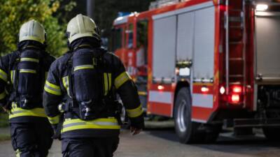Feuerwehrleute in Schutzkleidung stehen vor einem roten Feuerwehrfahrzeug bei Nacht