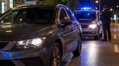 KI-Symbolbild mit Pkw im Vordergrund und Polizeifahrzeug mit Blaulicht bei Nacht