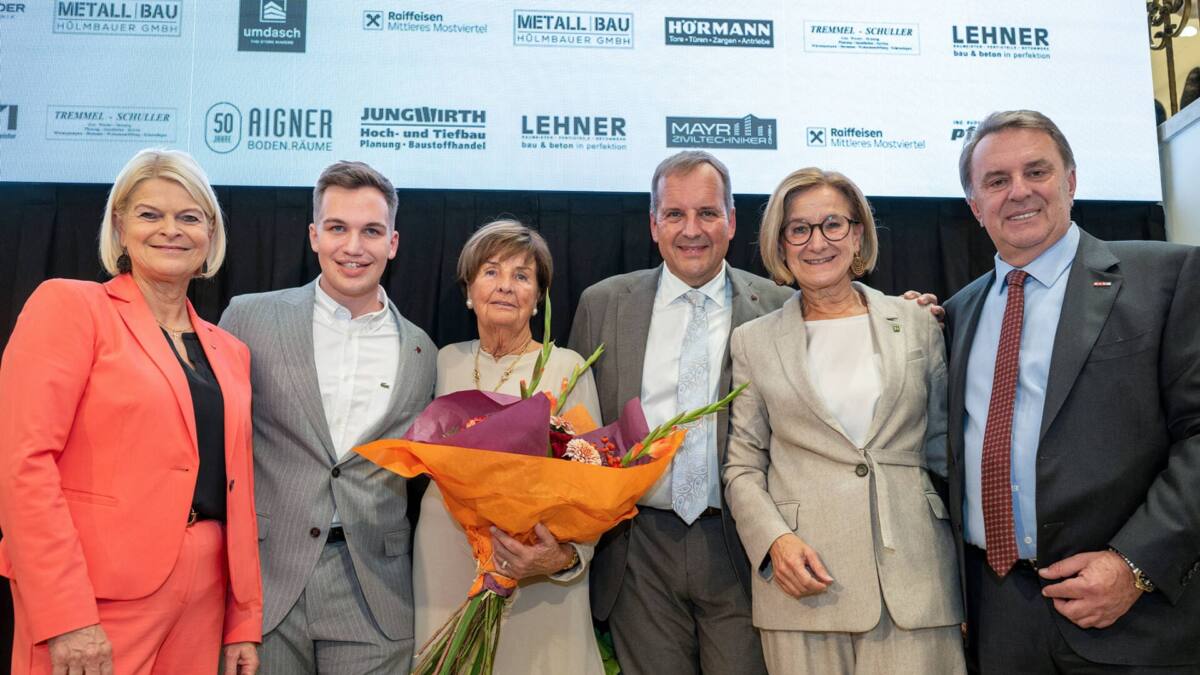 Eine Gruppe posiert mit einem Blumenstrauß vor einer Wand mit Firmenlogos.
