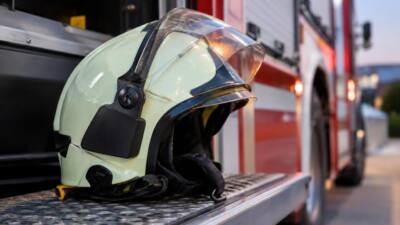 Ein Feuerwehrhelm liegt auf einer Trittfläche vor einem roten Einsatzfahrzeug.
