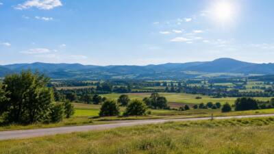 Sonnige Landschaft mit Feldern, bewaldeten Hügeln und blauem Himmel