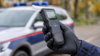 KI-Symbolbild: Eine behandschuhte Hand hält ein Atemalkoholmessgerät vor einem unscharfen Fahrzeug.