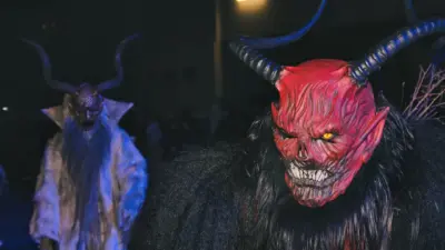 Nahaufnahme einer rot maskierten Krampusfigur mit Hörnern, dahinter eine weitere Gestalt.
