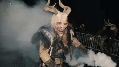 Eine gehörnte Krampusfigur tritt bei dichtem Rauch vor Absperrgittern auf.