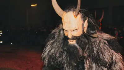 Ein Krampus mit großer Maske, Hörnern und zotteligem Fellkostüm bei einem nächtlichen Lauf.